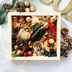 Gourmet gift box with assorted foods and a bottle of wine on a decorative surface.
