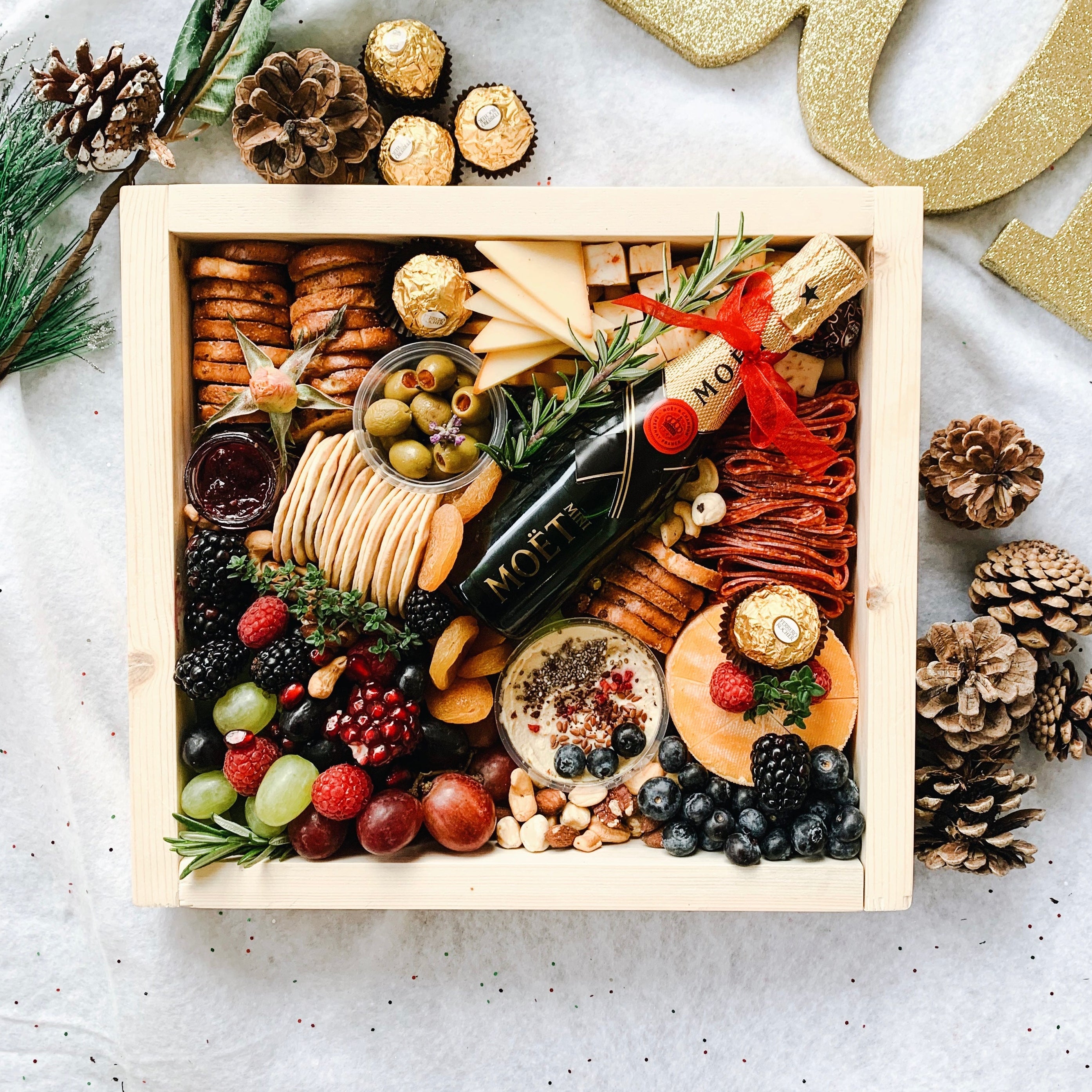 Gourmet gift box with assorted foods and a bottle of wine on a decorative surface.
